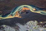 Detail eines bunten Gletscherflusses in Island, wie er sich über dunklen Sand seinen Weg in Richtung Ozean bahnt.